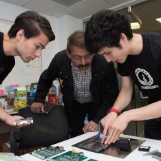 两个 students and Prof Gokli look at circuit boards on table